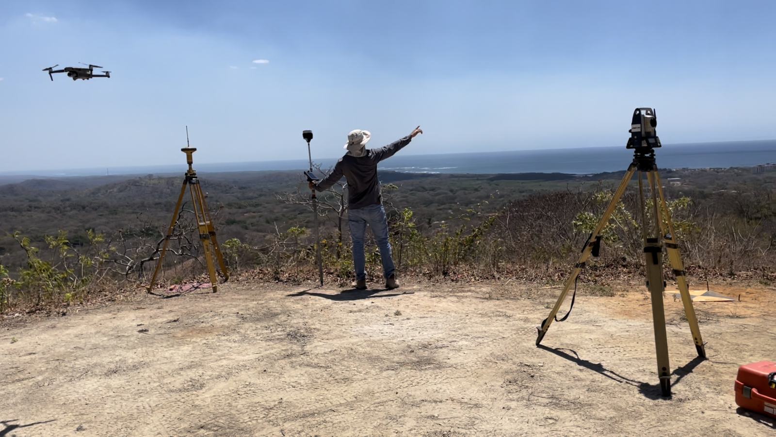 Equipo de campo con un dron en vuelo y receptores GNSS montados sobre trípodes en un cerro